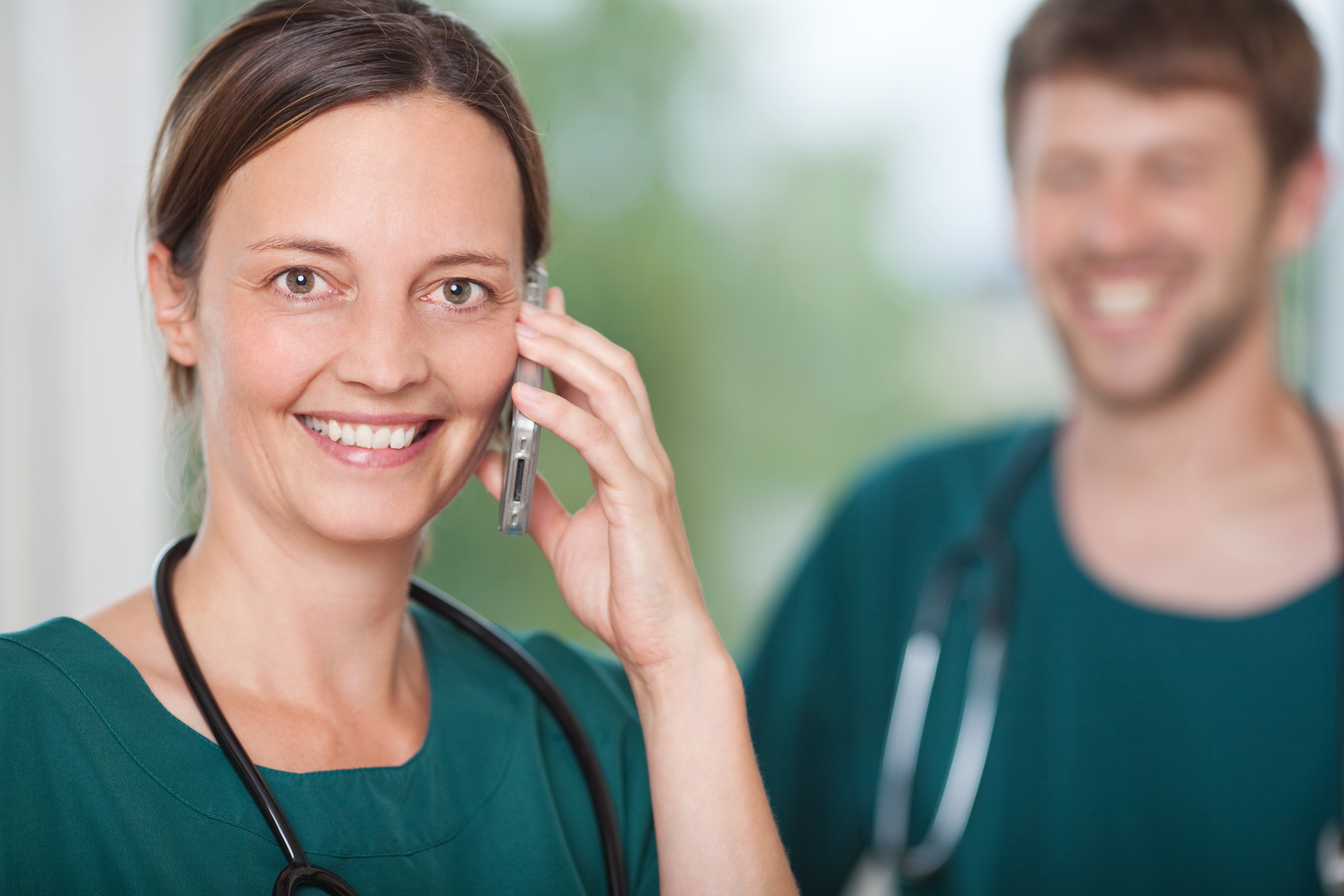 Lächelnde Ärztin mit Stethoskop telefoniert in der Arztpraxis - Symbol für moderne Patientenkommunikation und den Einsatz von KI-Telefonassistenten im Gesundheitswesen