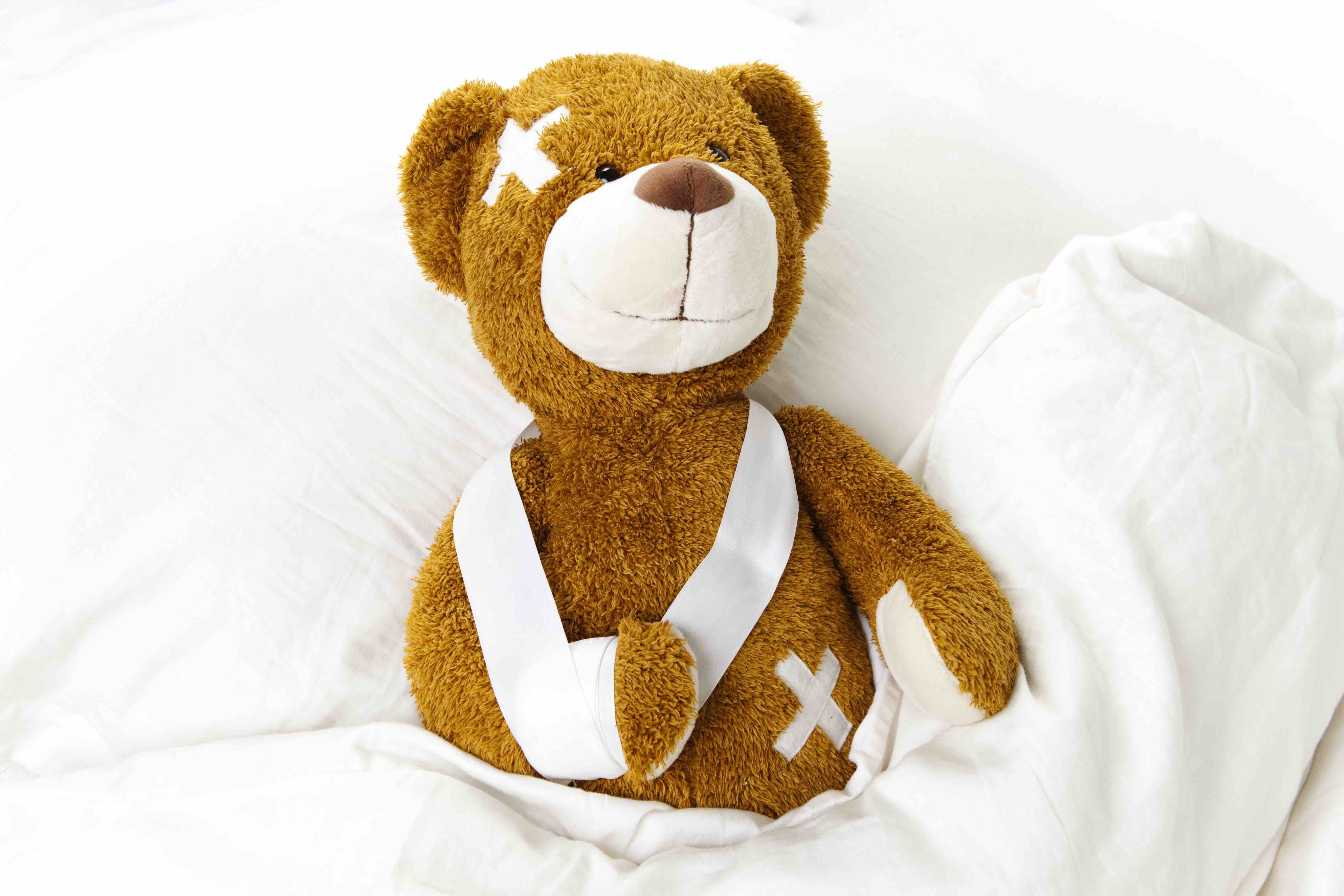 Plüsch-Teddybär mit Verband und Pflastern liegt im weißen Bett - Kinderfreundliche digitale Arztpraxis